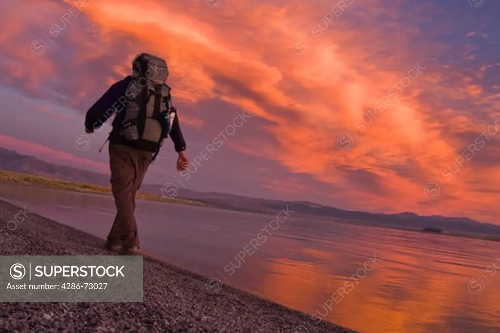  A man hiking along the shore of Mono Lake with reflecting water and clouds in California