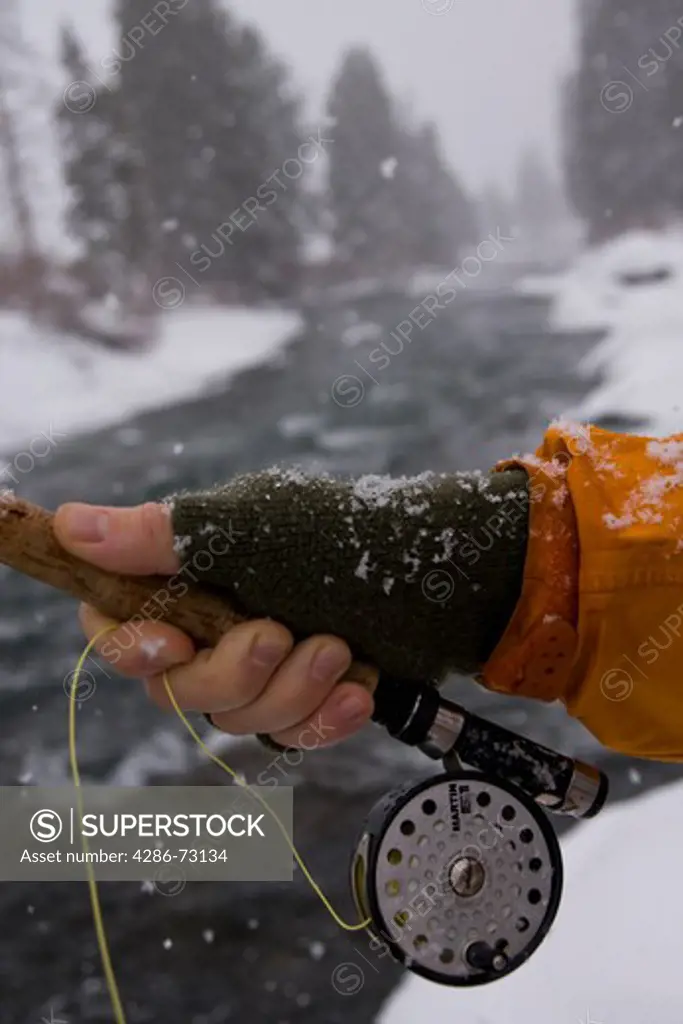 A close-up of a reel and hands of a man fishing on a snowy winter day on the Truckee River in California
