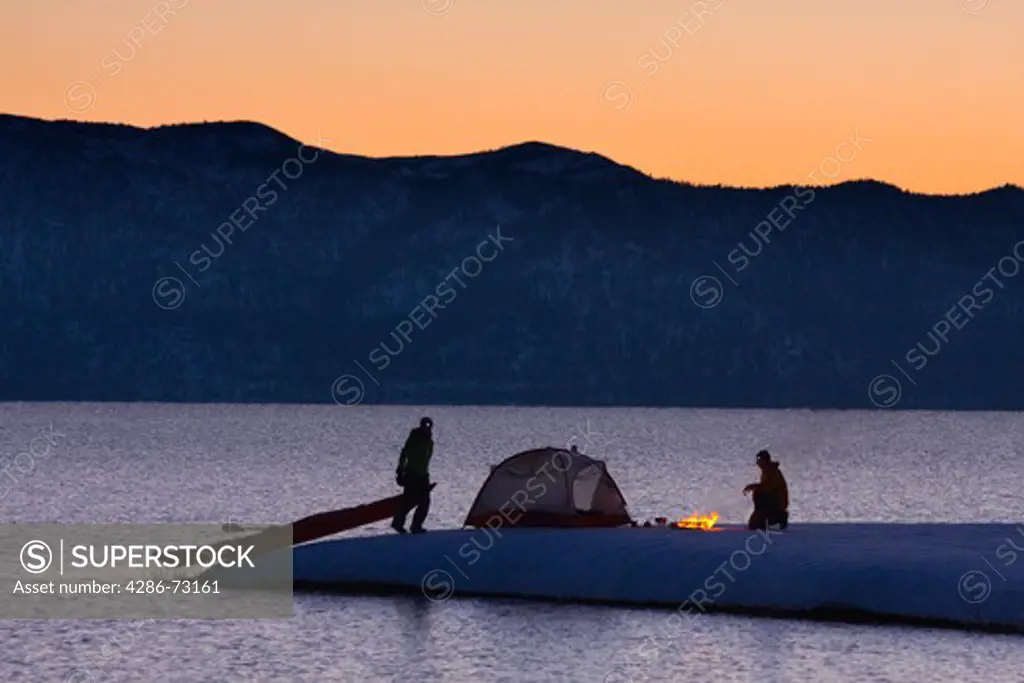 A man and a woman sea kayak camping on the shore of Lake Tahoe California in winter at sunrise