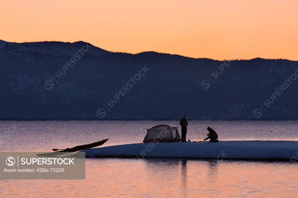 A man and a woman sea kayak camping on the shore of Lake Tahoe California in winter at sunrise