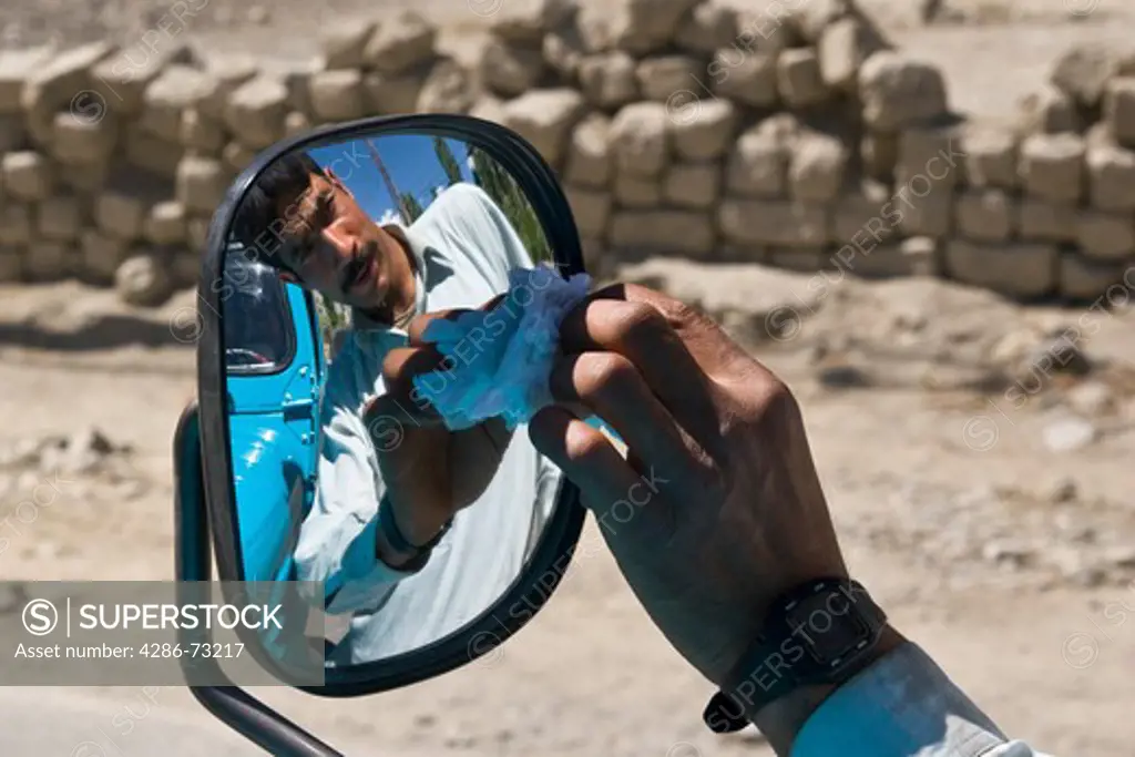 A portrait of a Pakistani man cleaning the mirror of his jeep