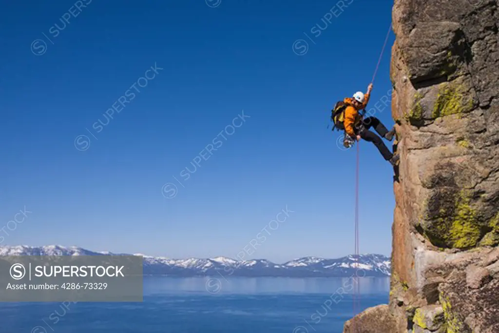  A man rappelling off a cliff above Lake Tahoe and the snowy Sierra mountains in Nevada
