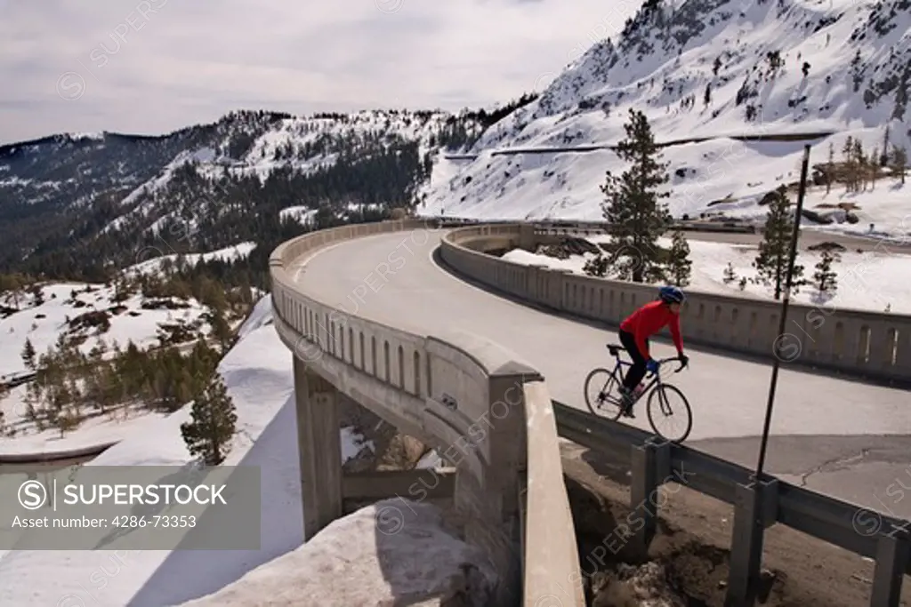  A man climbing uphill on a bicyle over a bridge in winter on Donner Summit in California