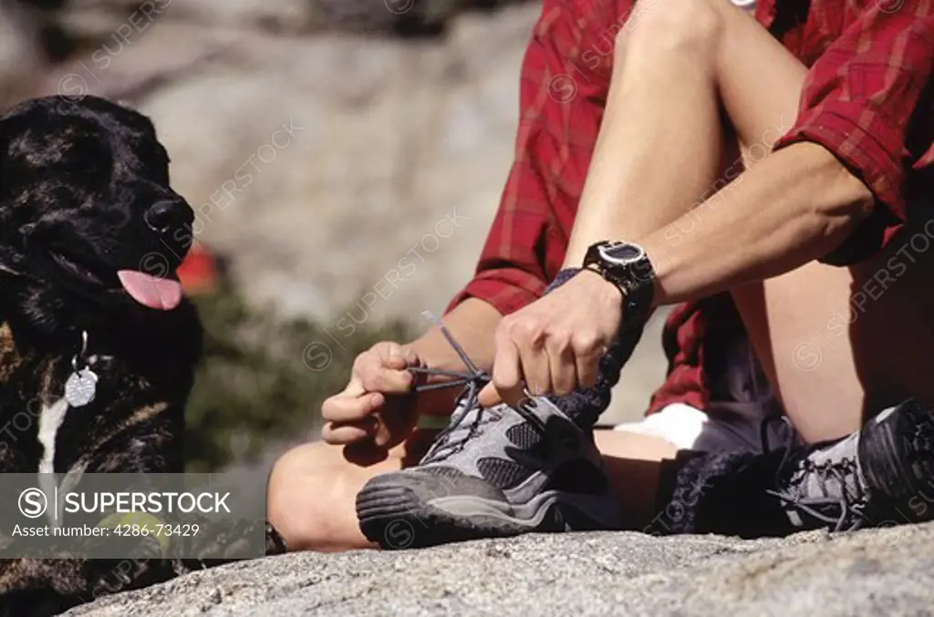 Young woman with dog tying shoes at Mount Judah in the Sierra mountains near Truckee, California, USA