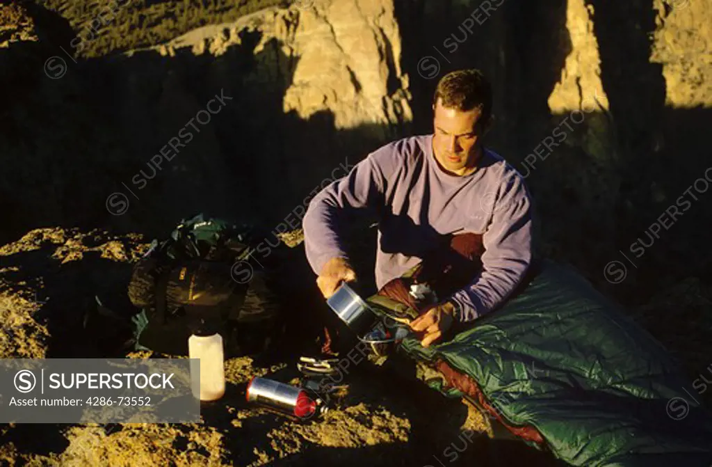 Man in sleeping bag pouring water in bowl at campsite at Smith Rock State Park in Oregon, USA