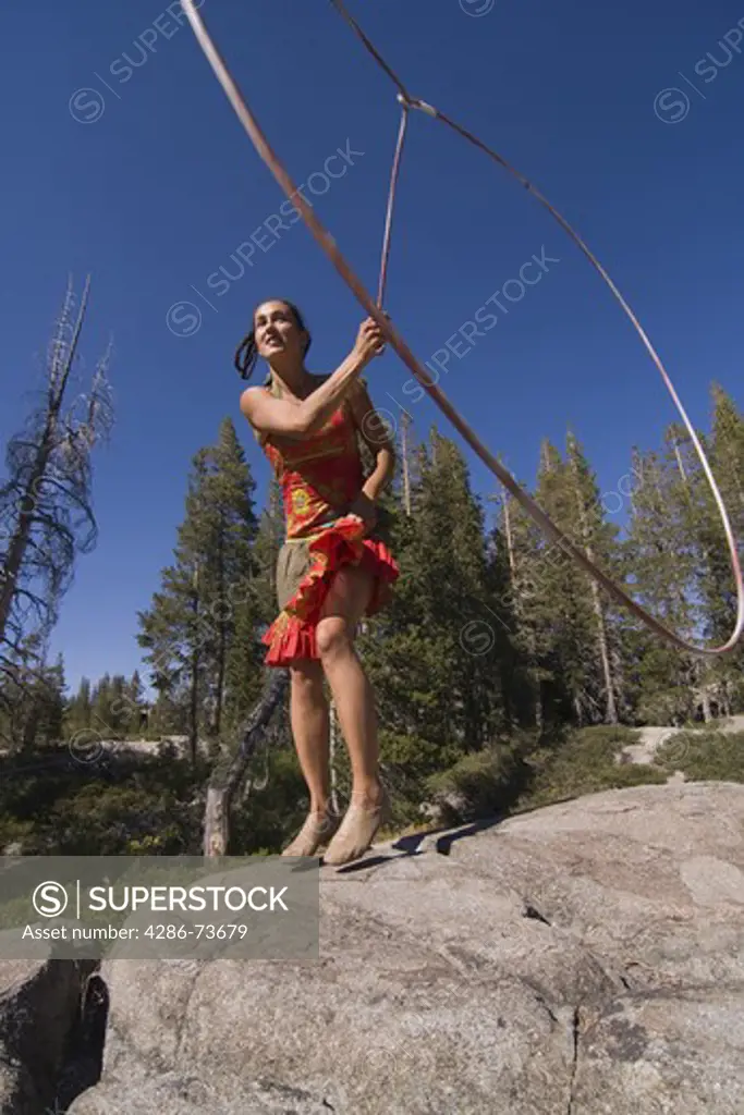 A woman performance artist jumping through a lariat in the forest on a blue sky day