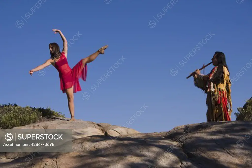 A Lakota Native American Indian warrior in traditional dress playing a love song on a flute to a dancing young maiden on Donner Summit near Truckee in California