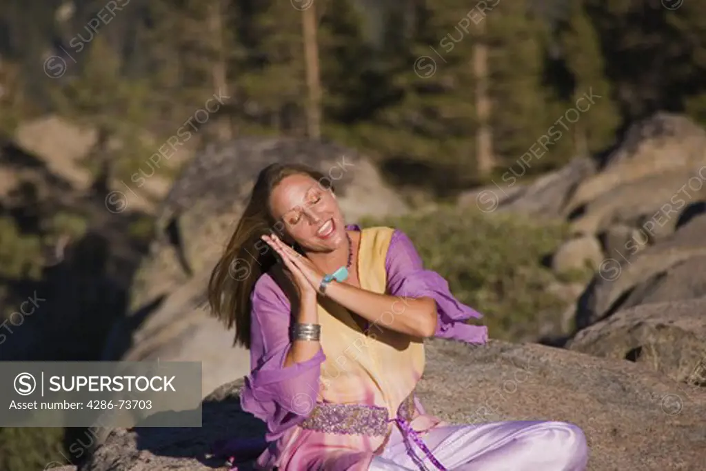 A woman in flowing robes sitting cross legged on a rock in the Sierra mountains  of California reciting a poem  