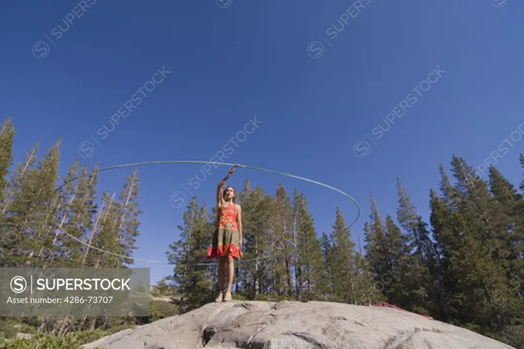 A woman performance artist with a lariat in the forest on a blue sky day