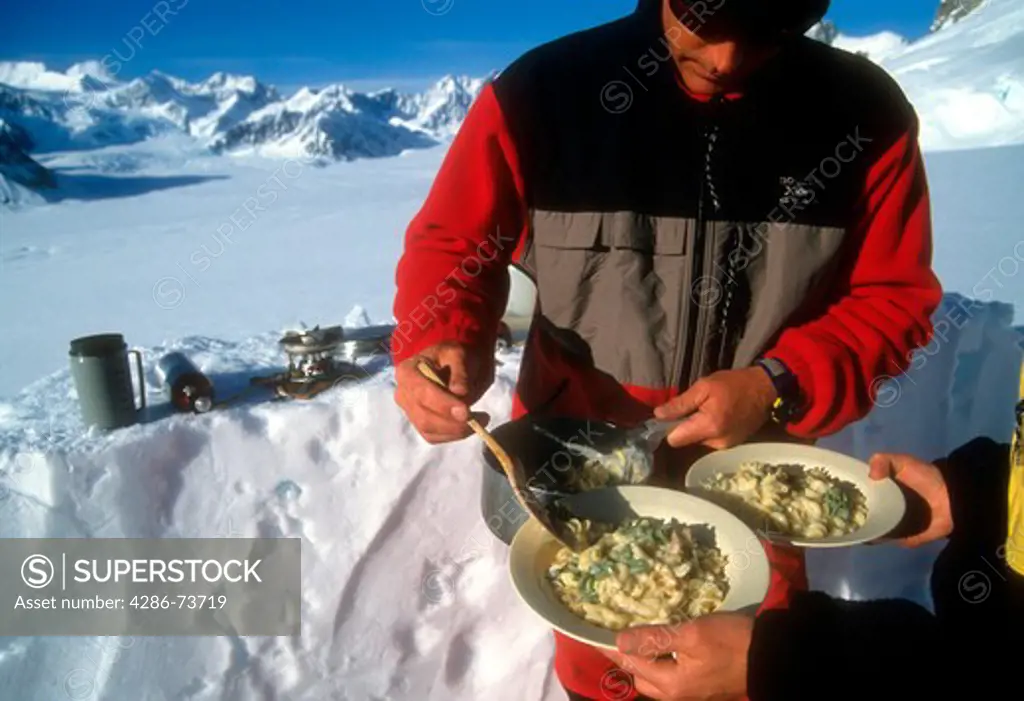 Man serving pasta at campsite, Ruth Gorge, Denali National Park, Alaska, USA 