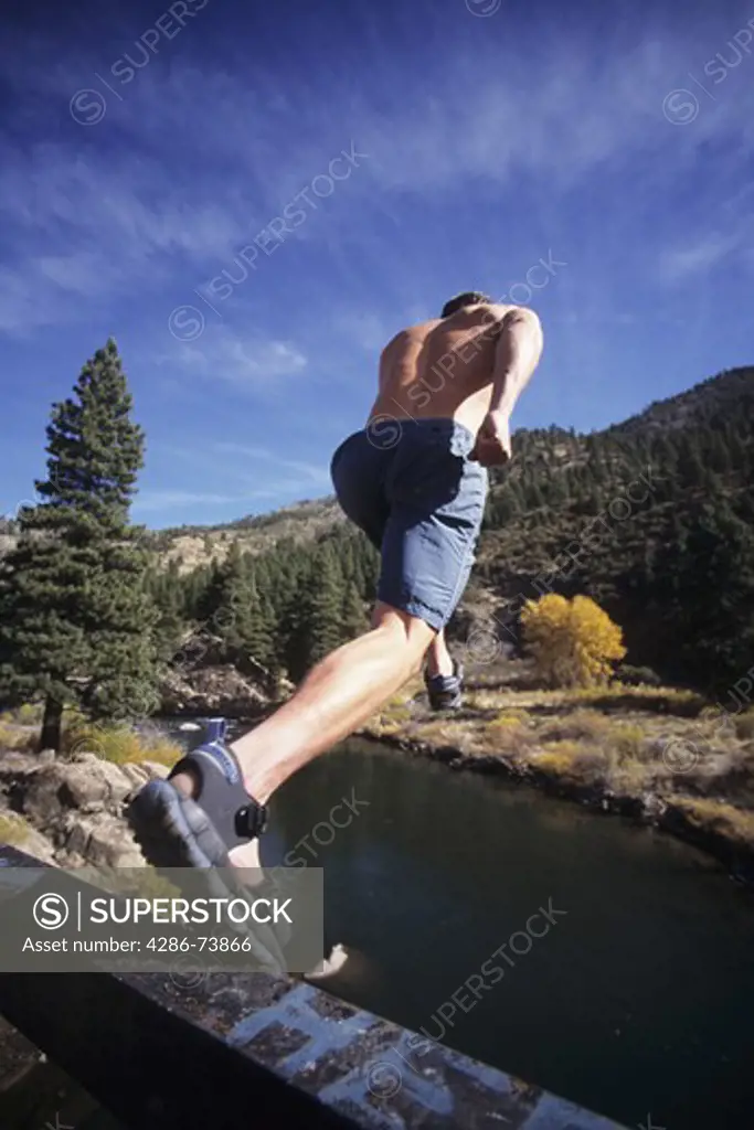 Young man jumping off ledge into the Truckee River, California, USA 