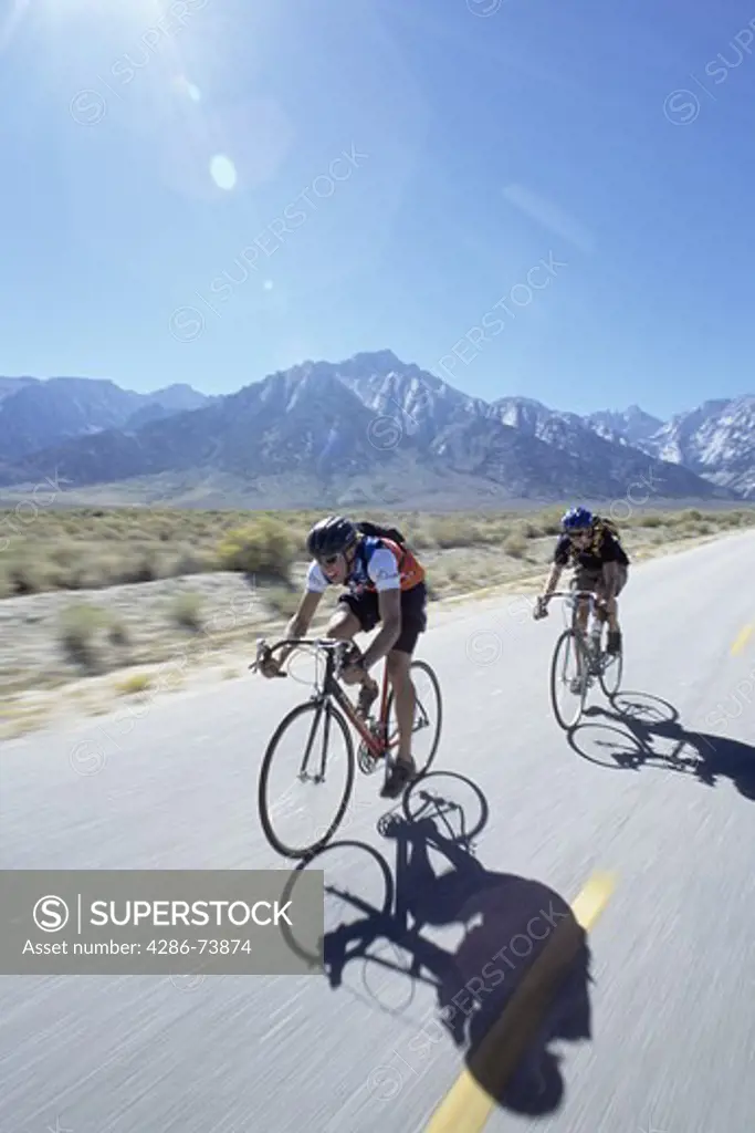 Two young men riding bicycles at a fast speed in front of Lone Pine Peak near Moutn Whitney in California