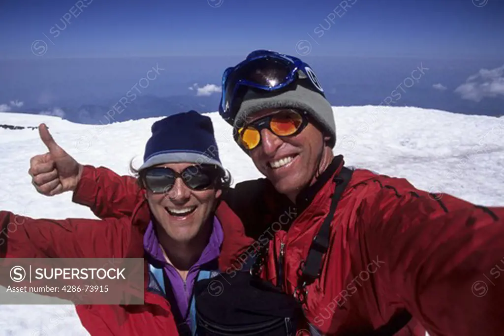 Two mountaineering friends celebrating giving the thumbs up on the summit of Mount Rainier in Washington