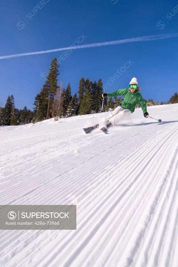 A woman alpine skiing on a freshly groomed slope on a blue sky day at Northstar ski resort near Lake Tahoe in California