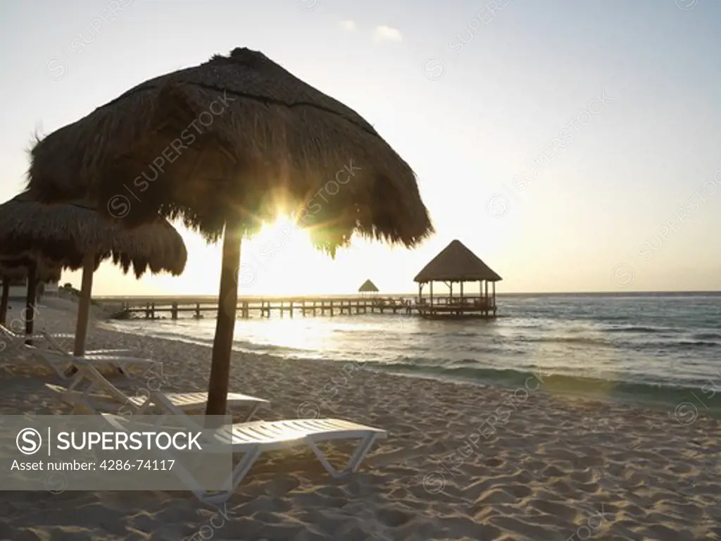 Mexico Quintana Roo Yucatan Peninsula Akumal Mayan Riviera, beach chairs under palapas at sunrise with pier and palapa jutting out to sea 