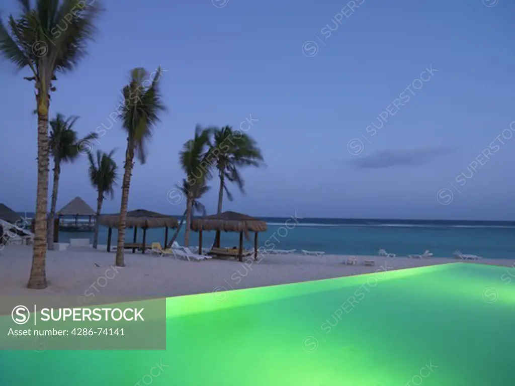 Mexico Quintana Roo Yucatan Peninsula Akumal Mayan Riviera,infinity pool illuminated by the edge of a beach with the sea in the background