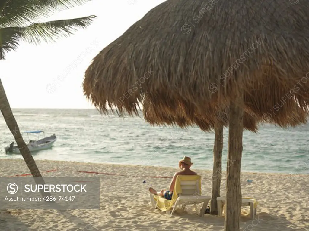 Mexico Quintana Roo Yucatan Peninsula Akumal Mayan Riviera,man sitting under a palapa at beach in bright sunlight
