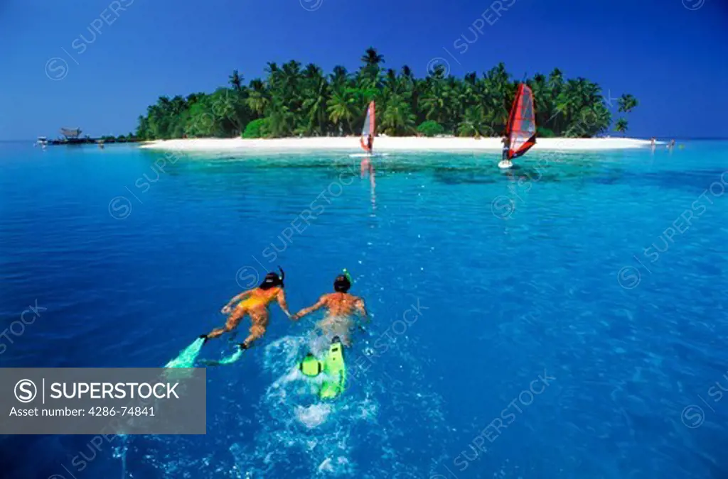 Couple snorkeling off Fihalhohi Island with windsailors in the Maldives
