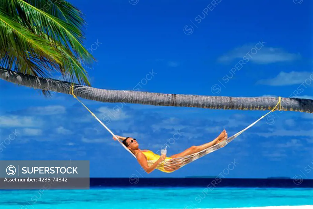 Woman relaxing in hammock under palm tree with tropical drink
