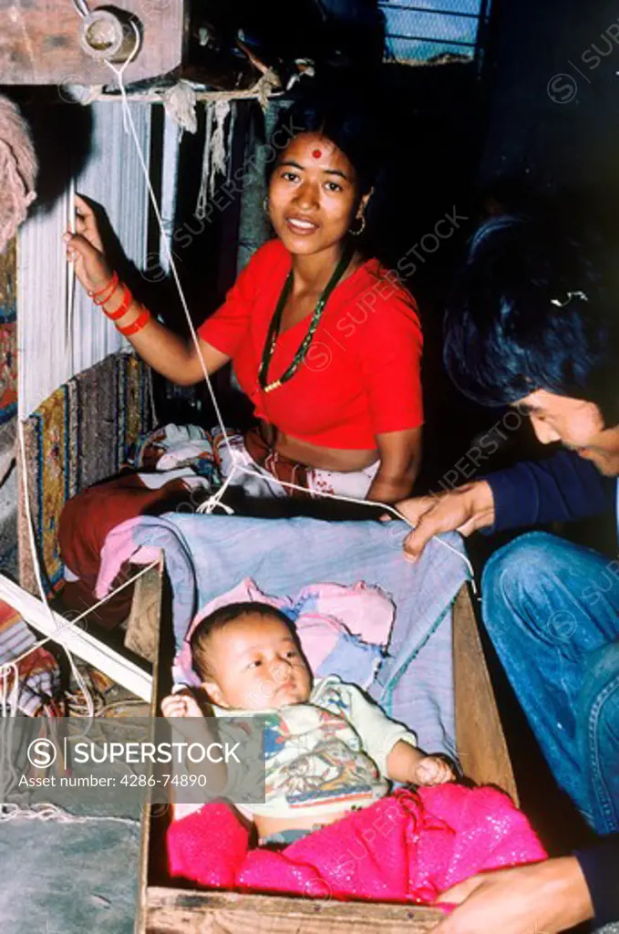 Napalese woman in weaving factory near Katmandu working with loom  while caring for her baby in wooden rocker