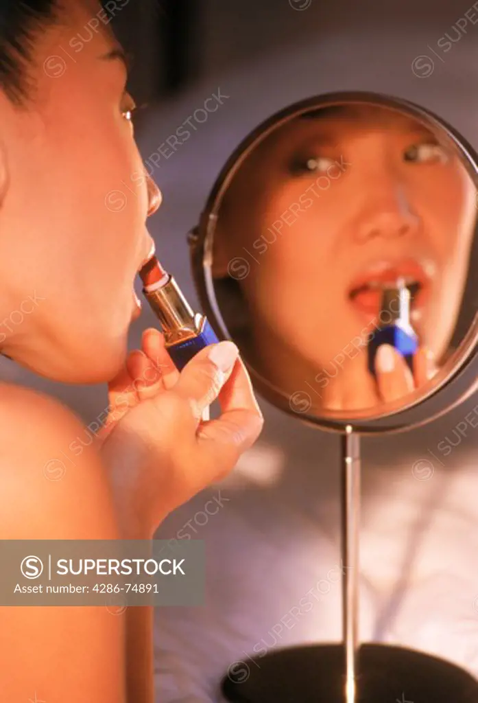 Asian woman applying lipstick using small mirror