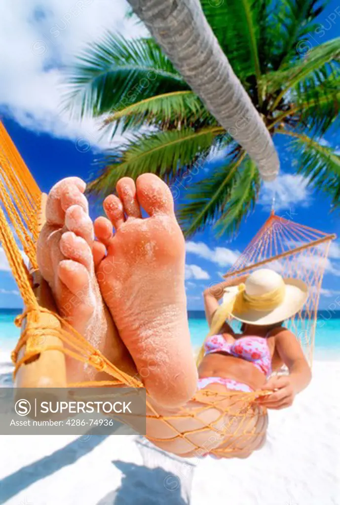 Woman with sandy feet resting in hammock under straw hat