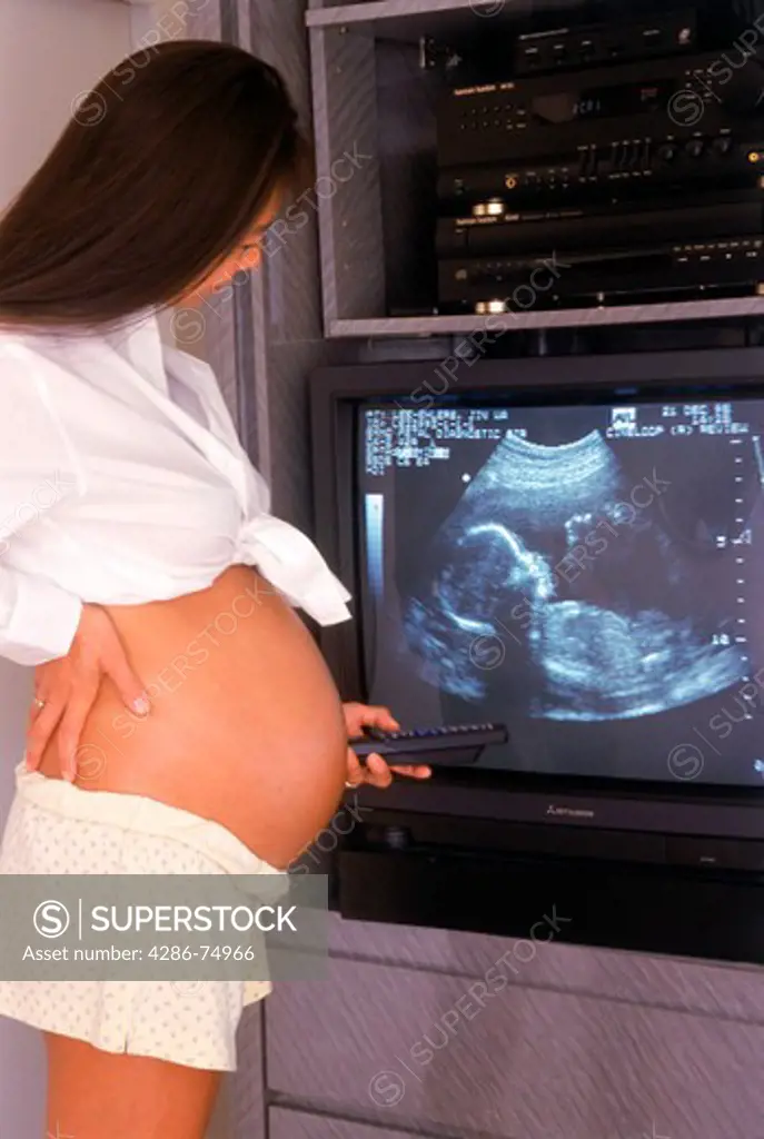 Pregnant mother proudly viewing her silhouetted fetus at home on ultrasound video