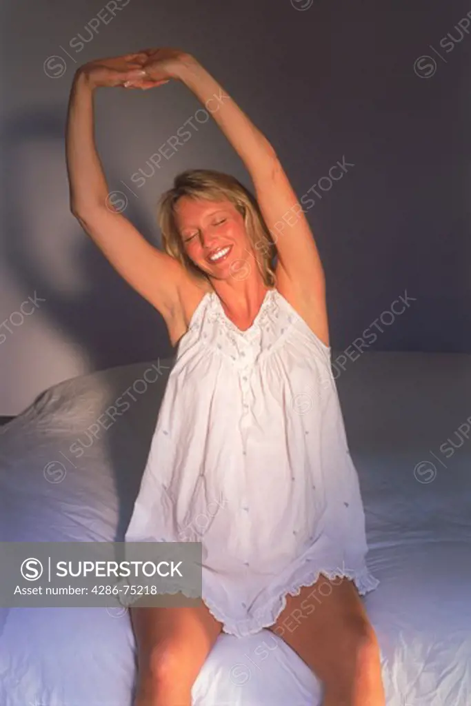 Pregnant women in nightgown on bed stretching in morning light 