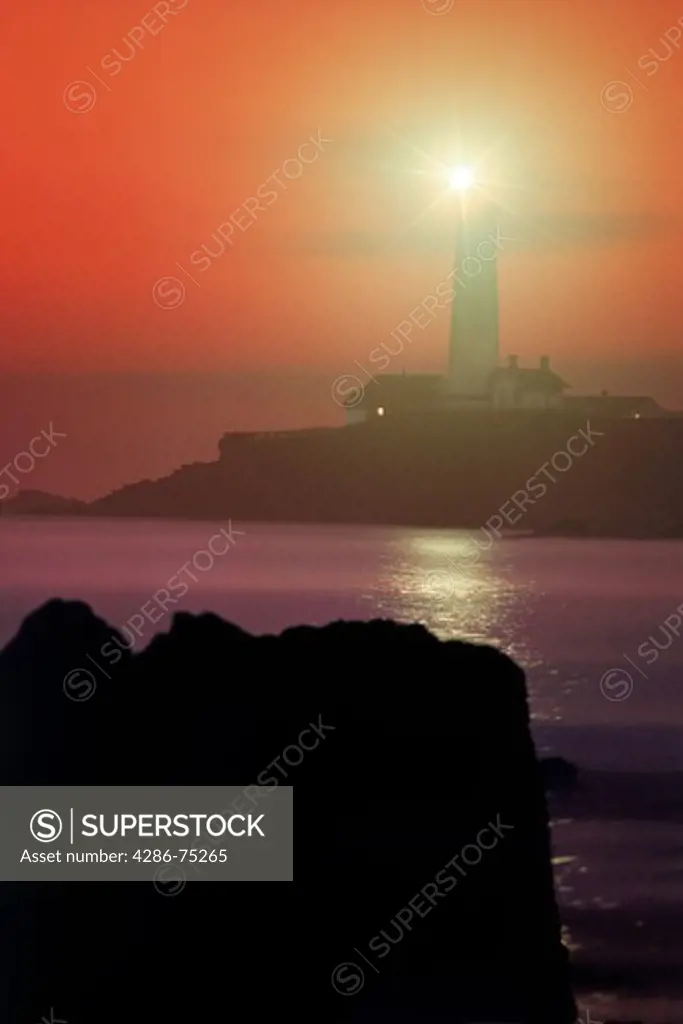 Pigeon Point Lighthouse sending beam over water to rocky shore at sunset near Santa Cruz California
