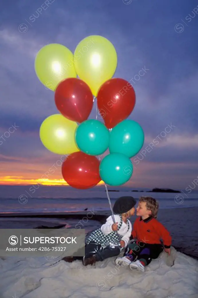 Children with colorful balloons on sandy shore at dusk in Laguna Beach California