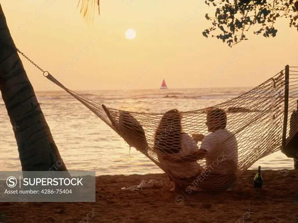 Couple sitting in beach hammock with bottle of Champagne at sunset
