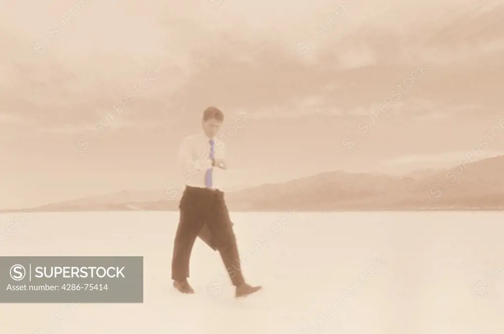 Businessman checking his watch while walking across barren desert landscape