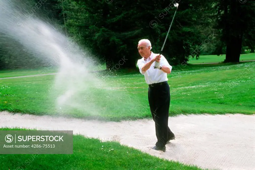 80 year old senior citizen blasting golf shot out of sand trap or bunker in Northern California