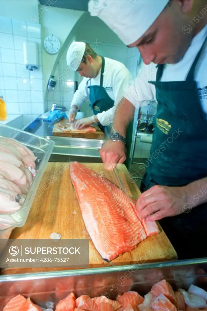Chef in restaurant kitchen filleting fresh salmon on wooden cutting board