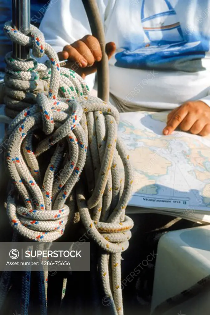 Man at helm of sailboat with compass, charts and rigging