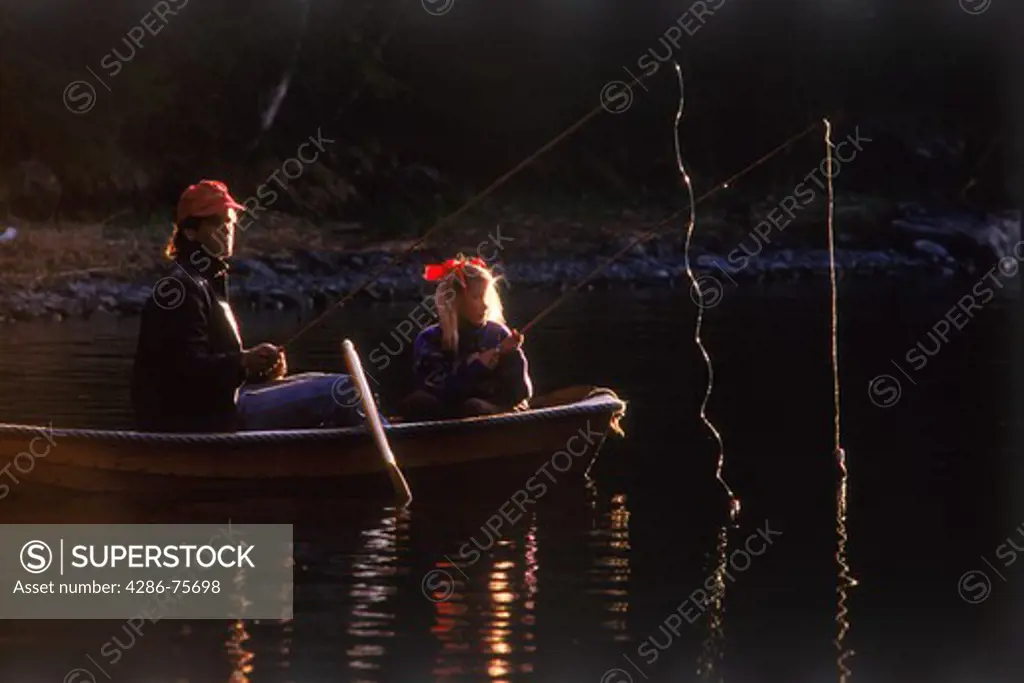 Father and daughter lake fishing from small rowboat in sunset light