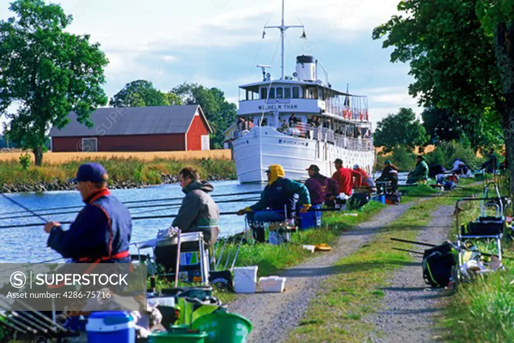 Passenger steamship passing line of pole fishermen while crossing Sweden on Gota Canal