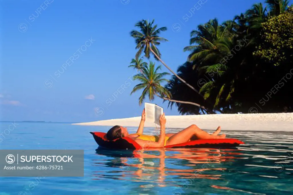 Woman relaxing and reading on air mattress in tropical paradise