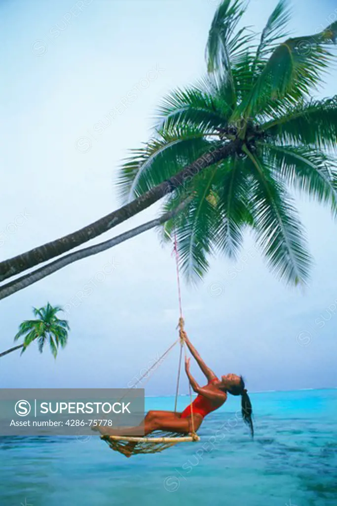 Woman relaxing in swing over aqua waters under palm tree
