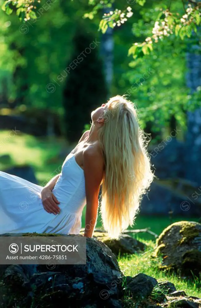 Blond woman in white dress relaxing alone in Swedish forest