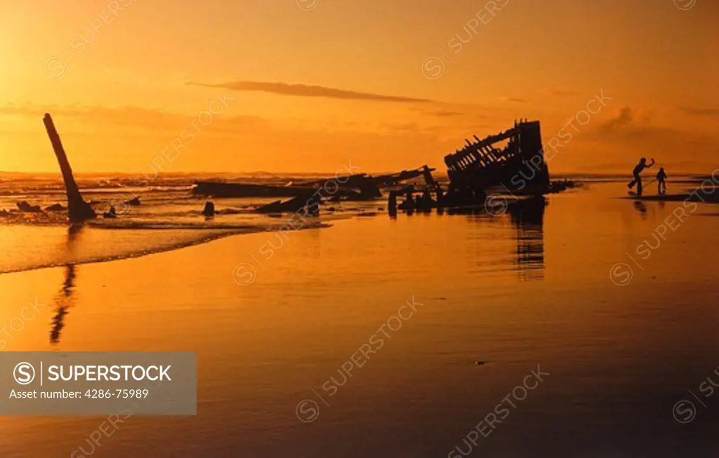 Mother and child silhouetted with old sunken ship Peter Iredale on Oregon coast at sunset