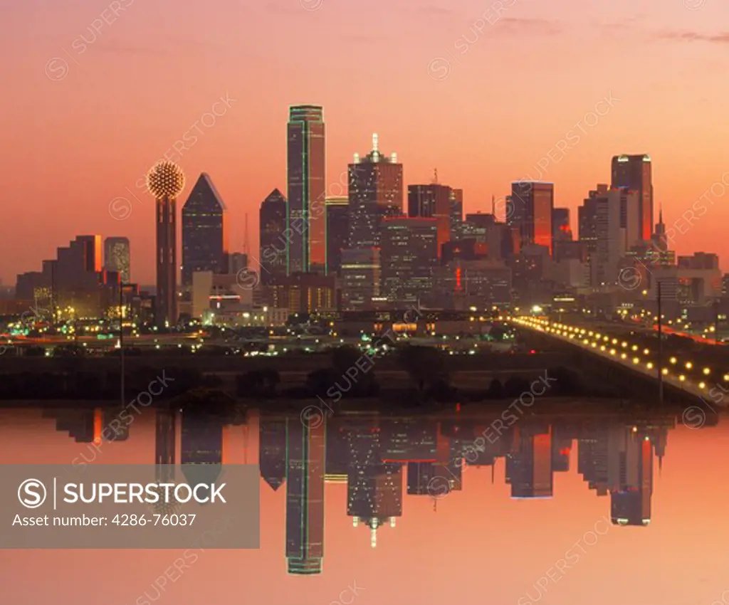 Dallas skyline at sunrise reflecting off glassy surface.