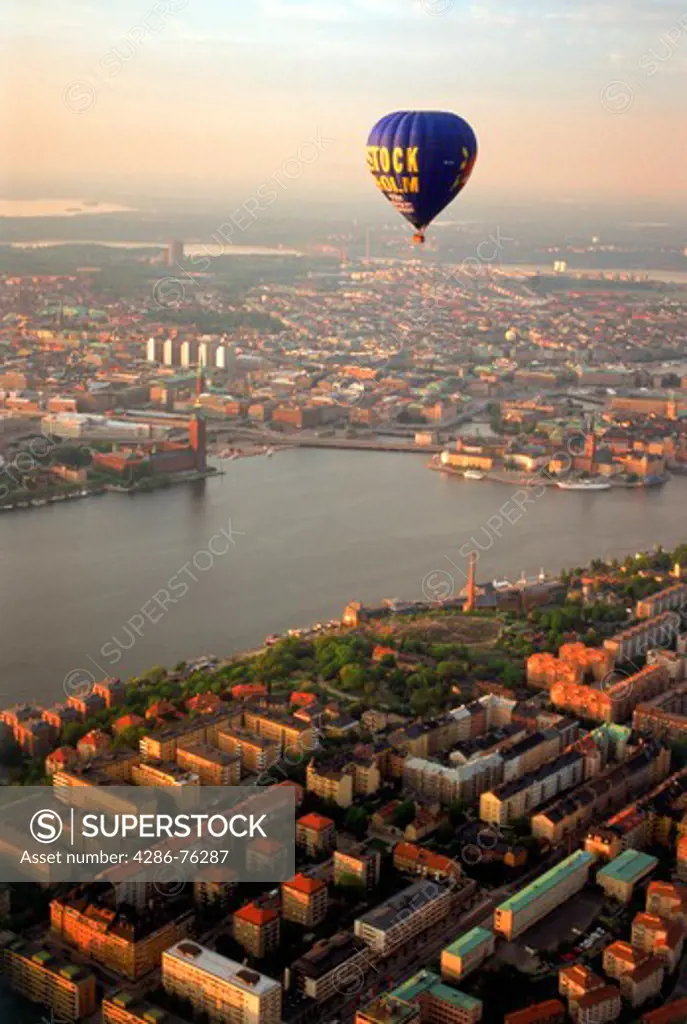 Hot air balloon floating over Sdermalm and islands of Stockholm with City Hall on Riddarfjarden waters at sunset
