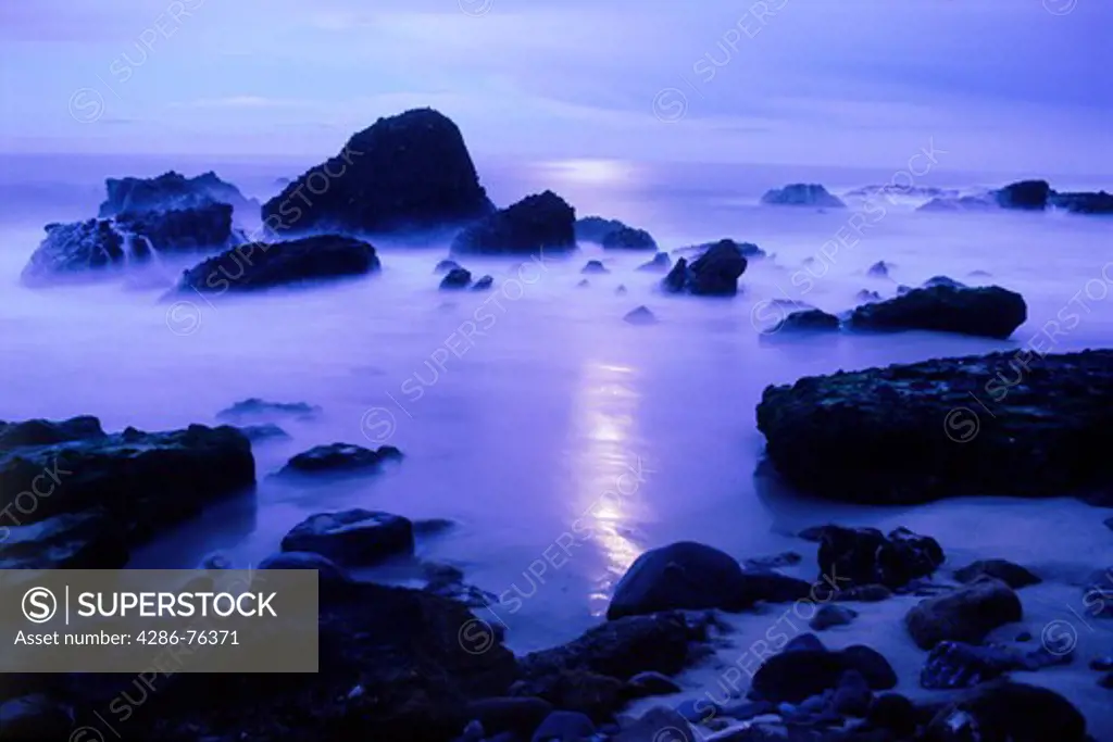Waves and moon light painting rocky shore at dusk at Woods Cove in Laguna Beach, California