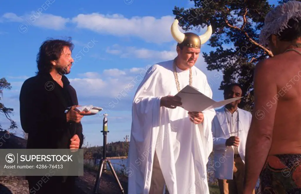 Big Viking priest with headgear and horns reading wedding vows during humorous wedding on island in Stockholm Sweden