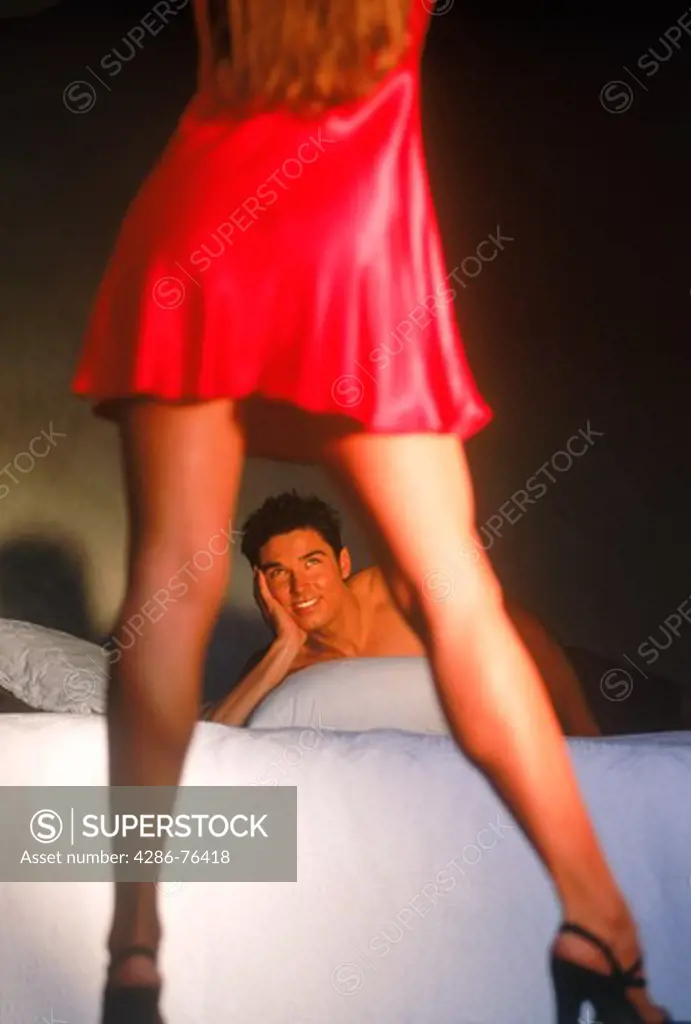Man on bed admiring his lady standing in red lingerie
