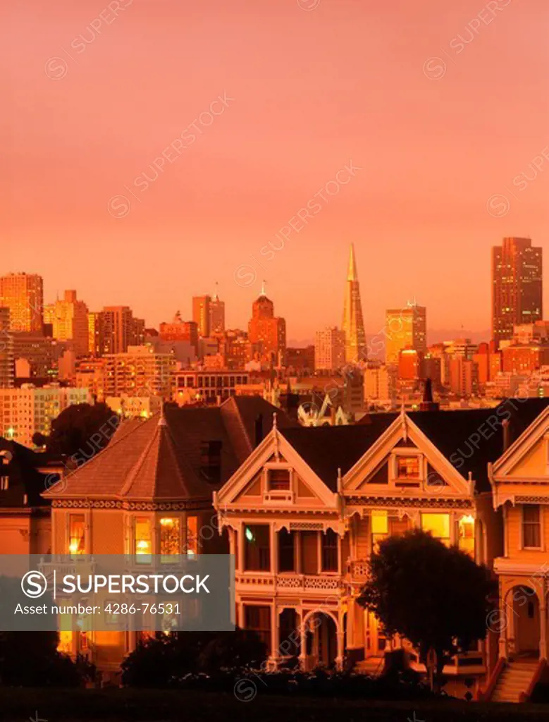 Victorian Houses on Steiner Street at dusk in San Francisco with city skyline beyond