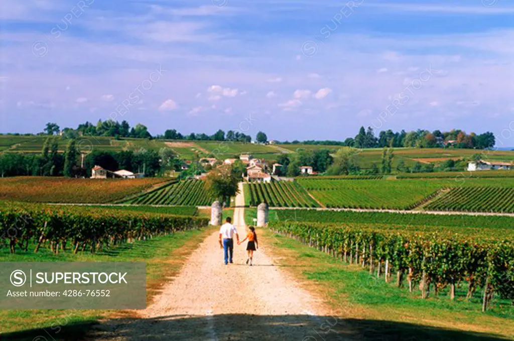 Father and daughter walking dirt road leading to Chateau Saint-Georges near St. Emilion in Bordeaux region of France