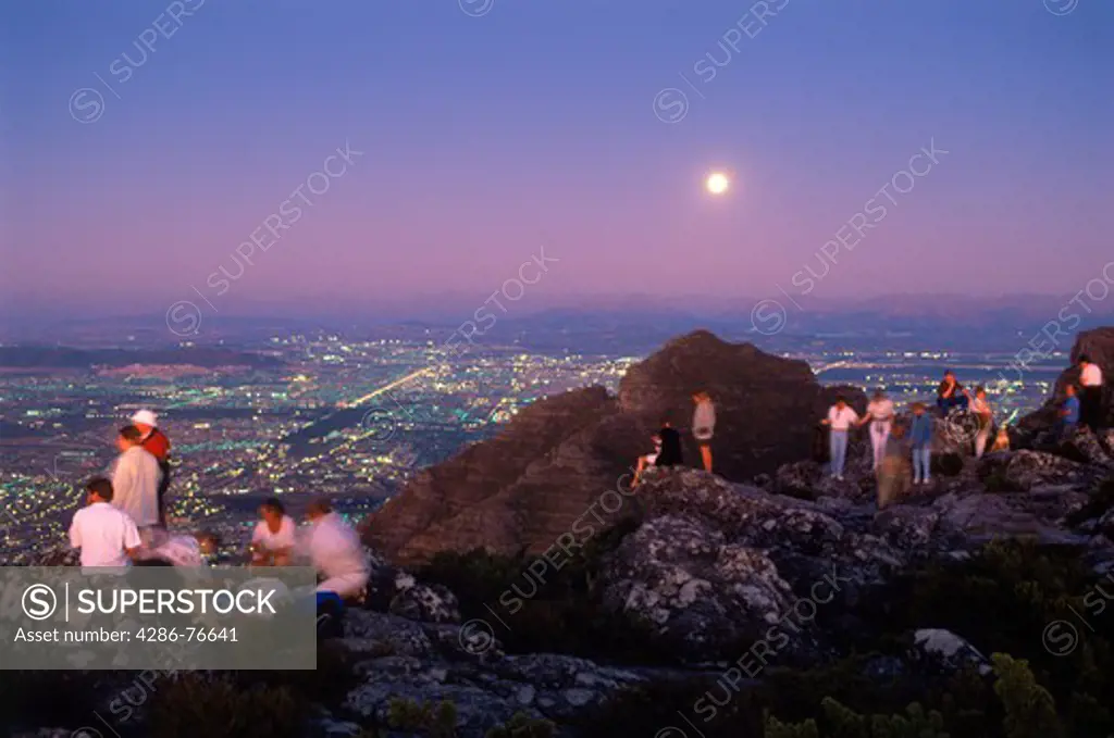 Visitors with food and drink watching sunset from top of Table Mountain above Cape Town under full moon