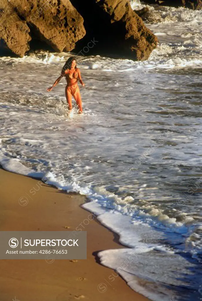 Woman walking along through shore waves near sunset in Laguna Beach California